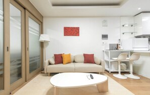 Una sala moderna con sofá, una mesa de centro y una cocina con refrigerador y microondas.
