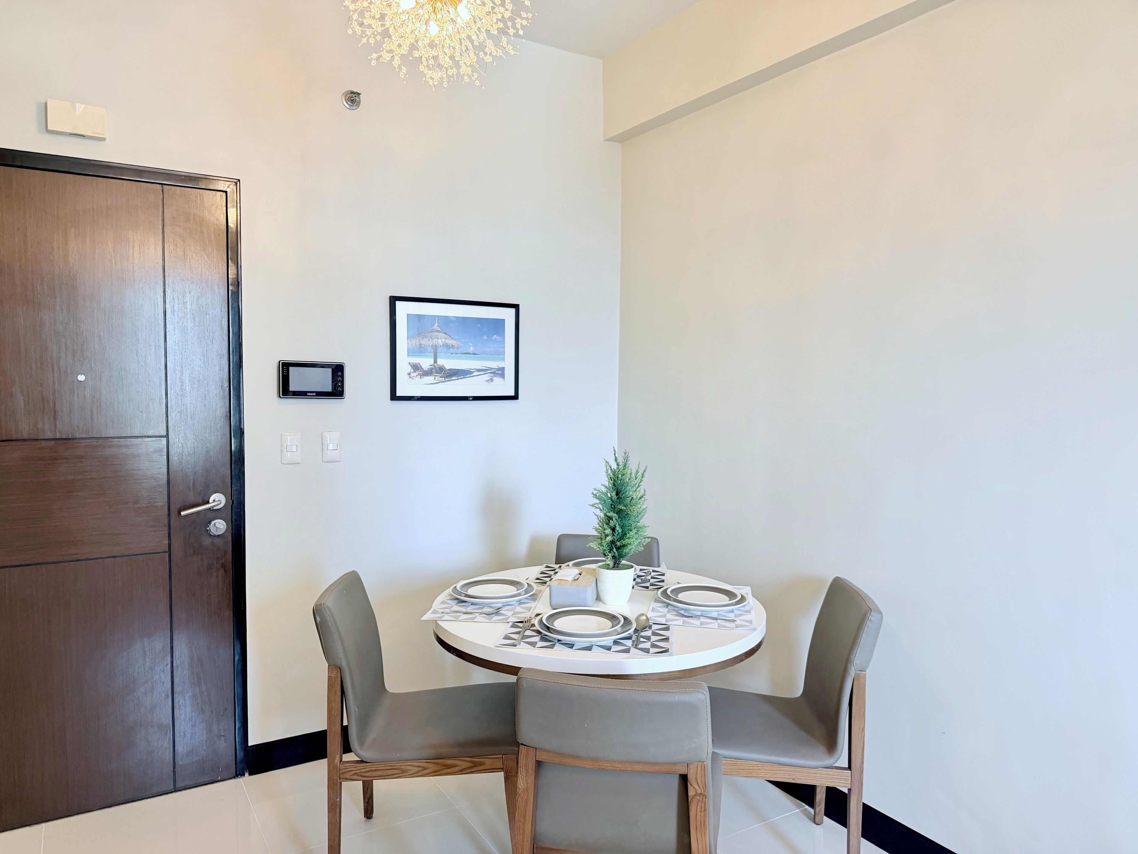 A dining area with a round table set for two, two chairs, a small potted plant, and a framed picture on the wall.