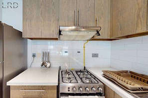 A kitchen with wooden cabinets, a white countertop, a gas stove, and a kettle. - Brand New and Modern 1BR Apartment (Dubai)