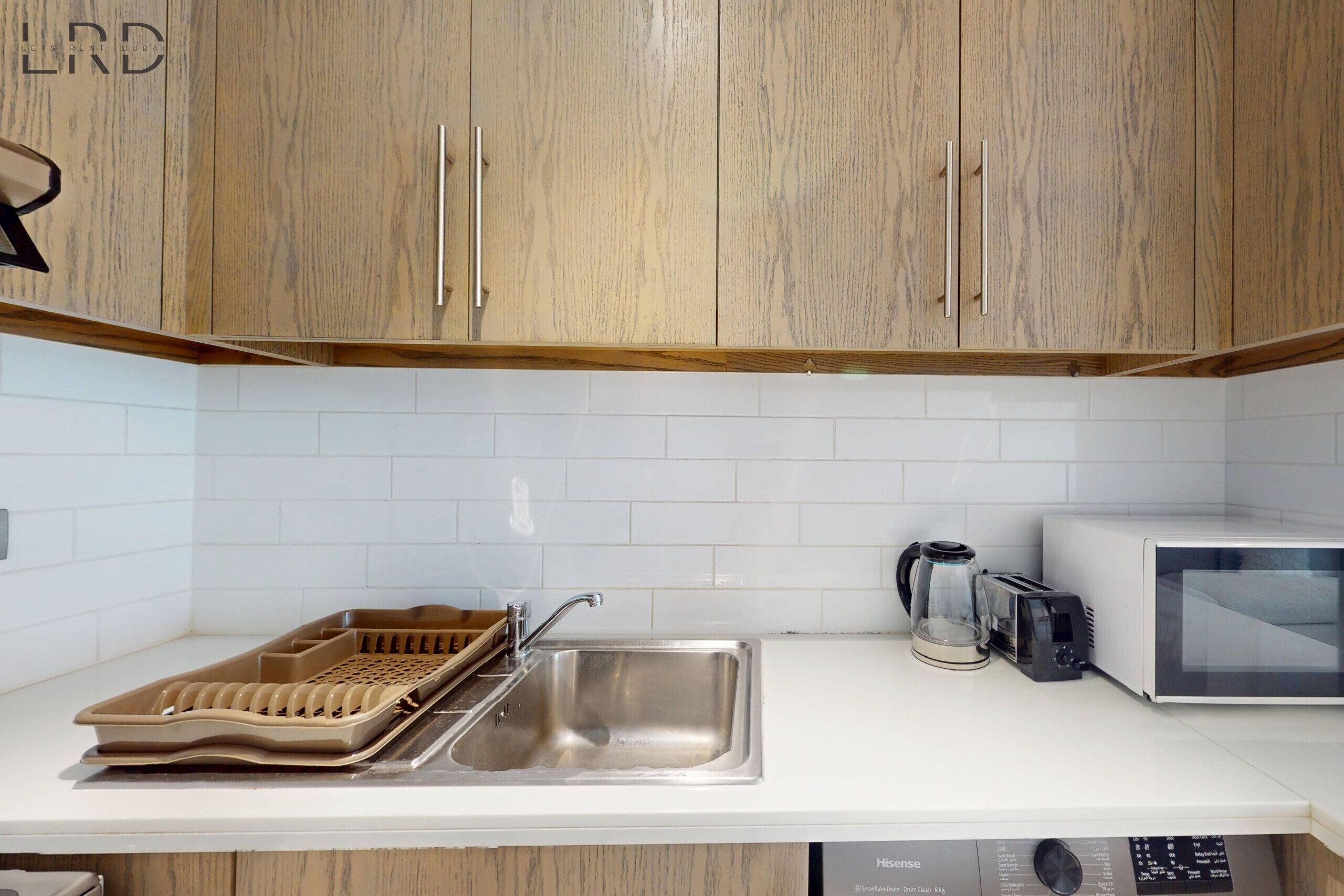 Una cocina con armarios de madera, un lavamanos de acero inoxidable, un tostador y un lavavajillas.