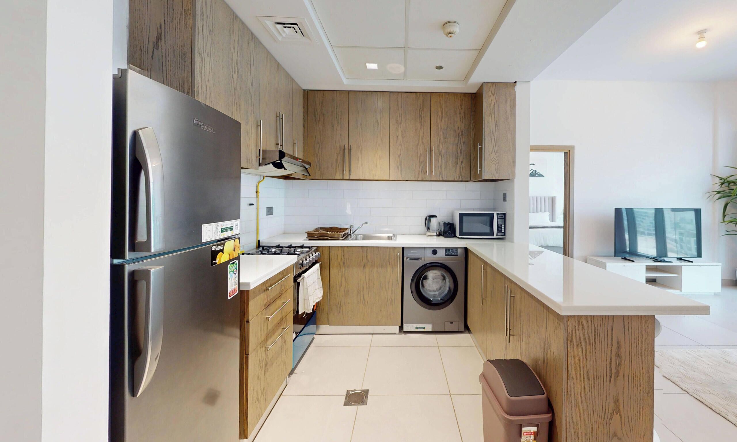 Una cucina moderna con mobili in legno, elettrodomestici in acciaio inossidabile, un forno a microonde e una lavatrice.
