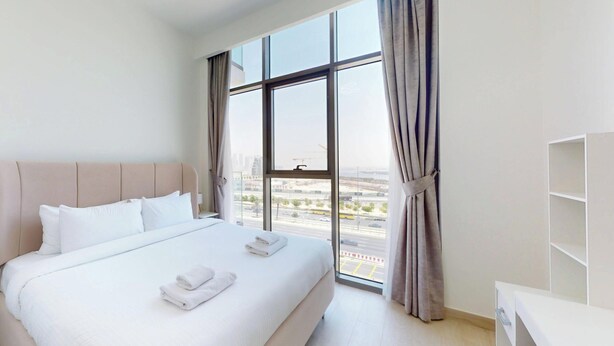 A hotel room with a large bed, a desk, and a view of the city through a large window.