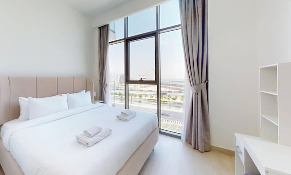 A hotel room with a large bed, a desk, and a view of the city through a large window.