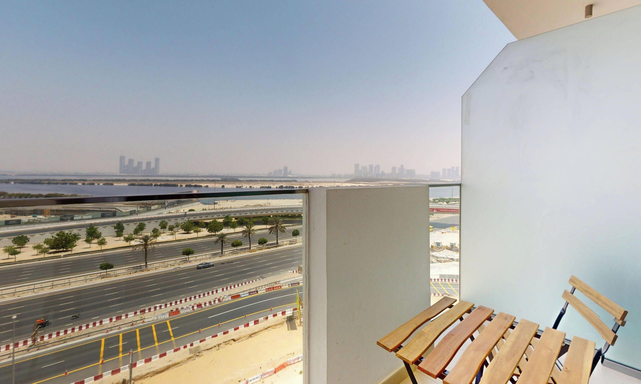 A view from a balcony with a table and chairs, overlooking a wide road with multiple lanes and a distant city skyline.