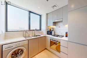 A modern kitchen with a built-in washer, a gas stove, and a microwave. - Charming 1BR with Canal View (Dubai)