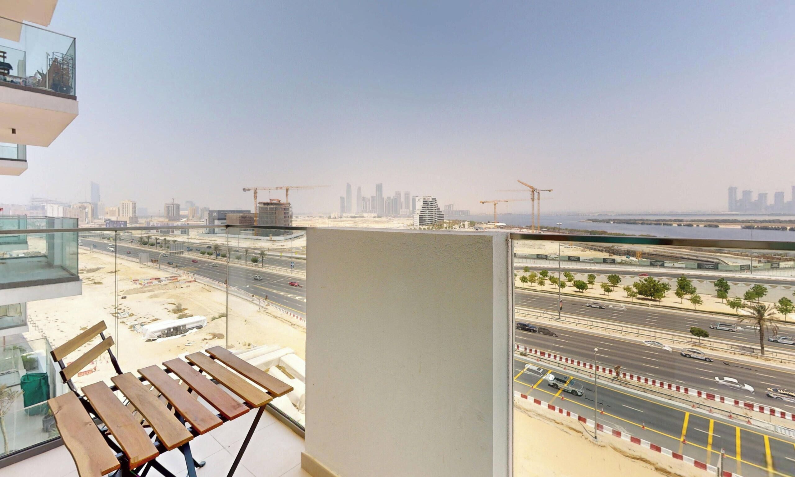 A balcony with a view of a cityscape, including a highway and construction cranes.
