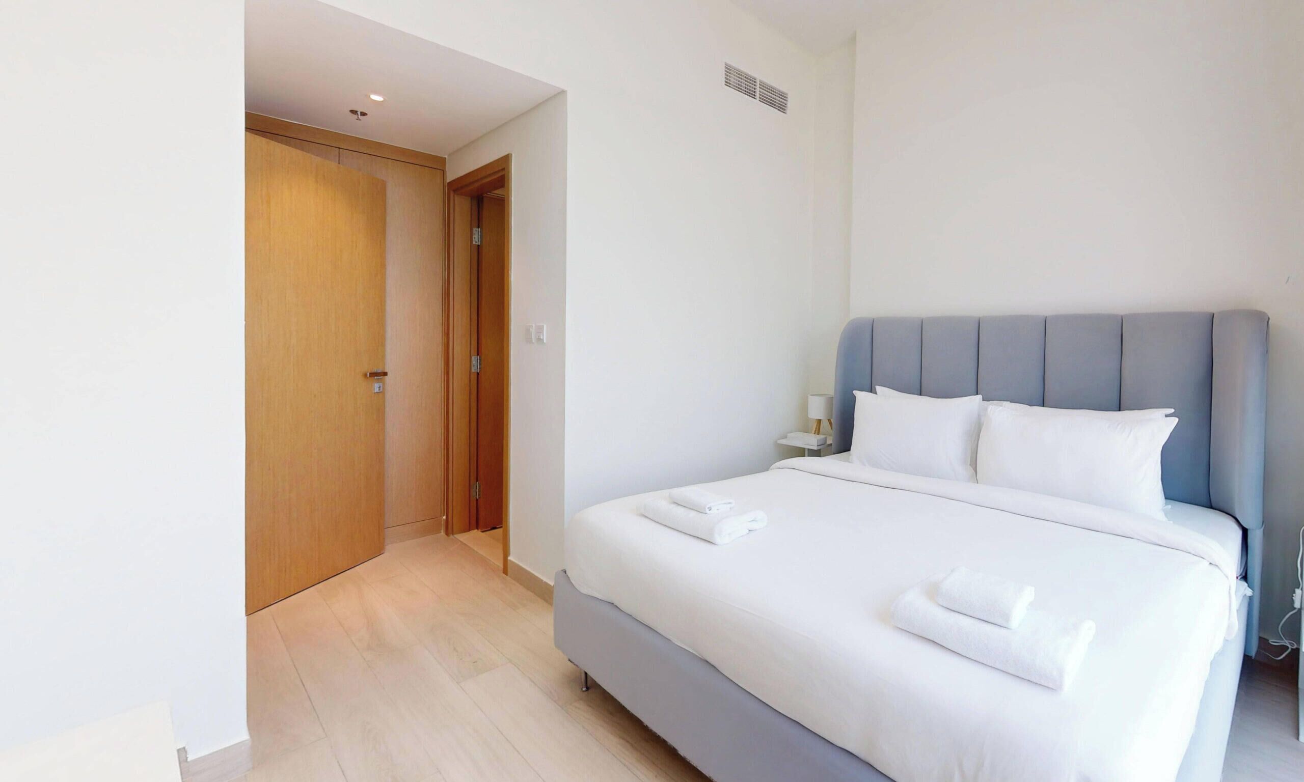 A hotel room with a bed, a nightstand, a lamp, and a wooden door.