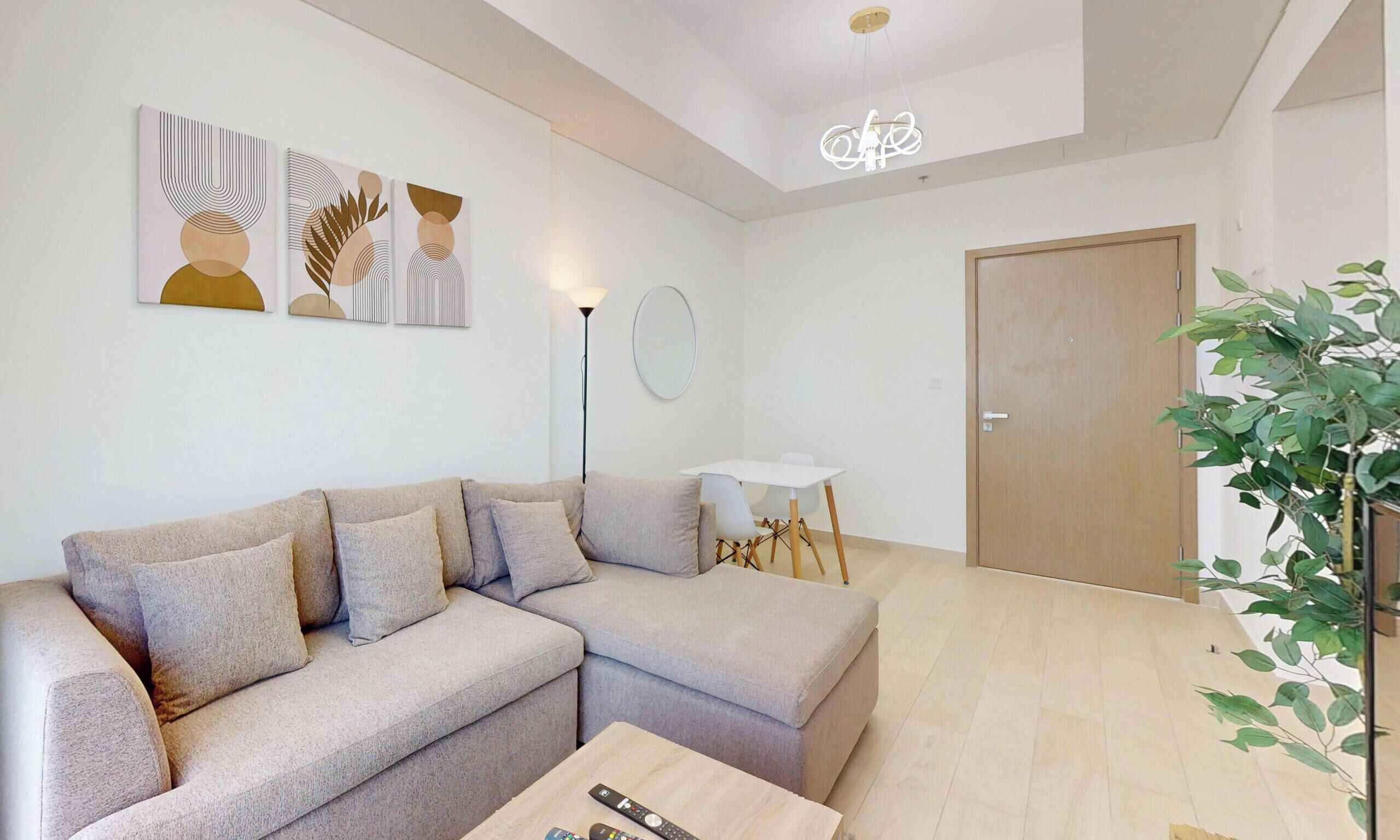 Una sala de estar con un sofá modular, una lámpara de pie, una mesita con un control remoto y una planta en maceta.