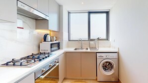 A compact kitchen with a gas stove, microwave, sink, and built-in washing machine. - Chic 1BR with Canal View (Dubai)