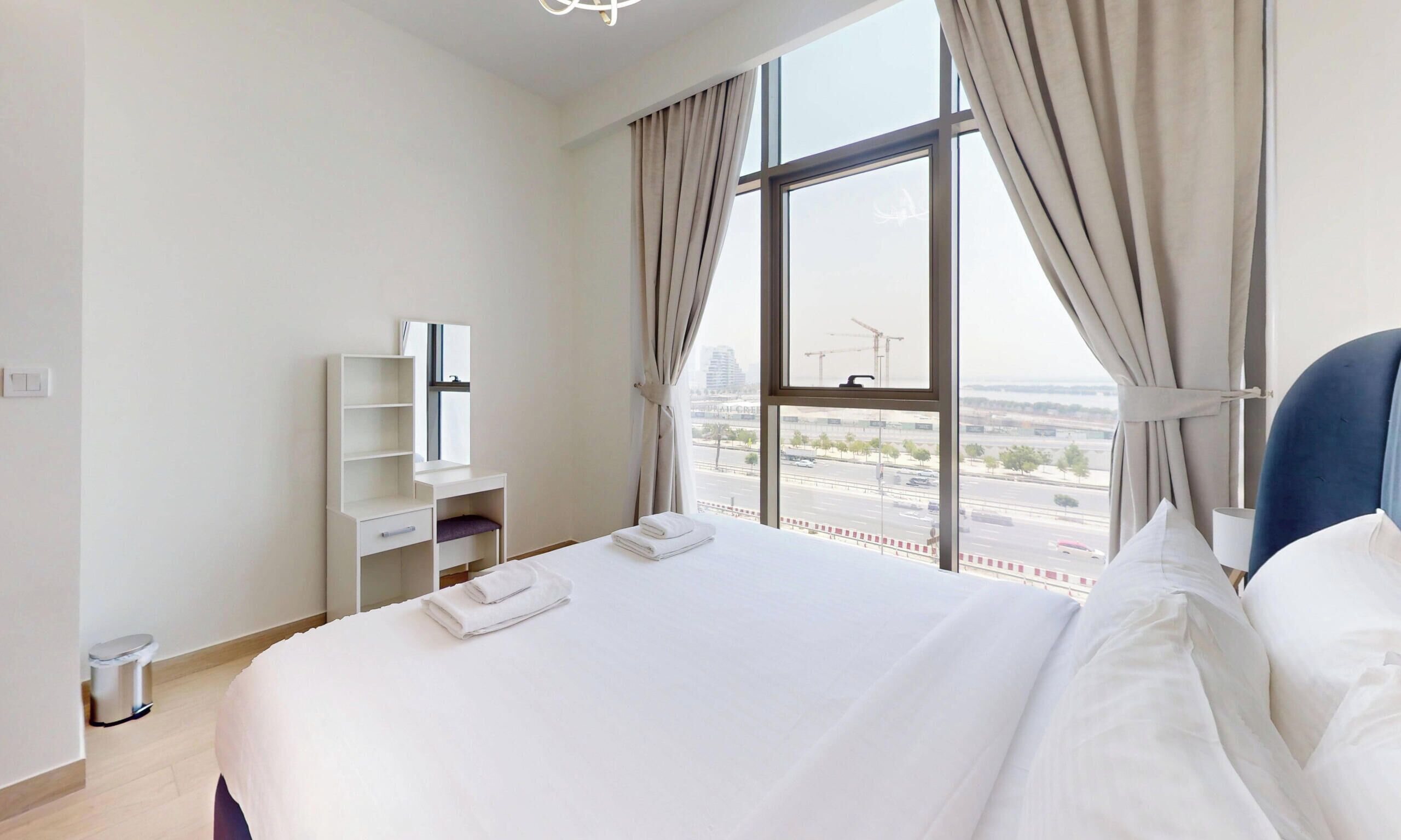 Een hotelkamer met een groot bed, een bureau, een stoel en uitzicht op de stads skyline.