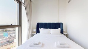 A hotel room with a large bed, white linens, a dark headboard, and a view of a cityscape through a large window. - Chic 1BR with Canal View (Dubai)