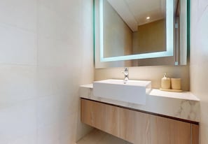 A modern bathroom with a white sink, wooden vanity, and a large mirror. - Cozy and Modern 1BR for 2 (Dubai)
