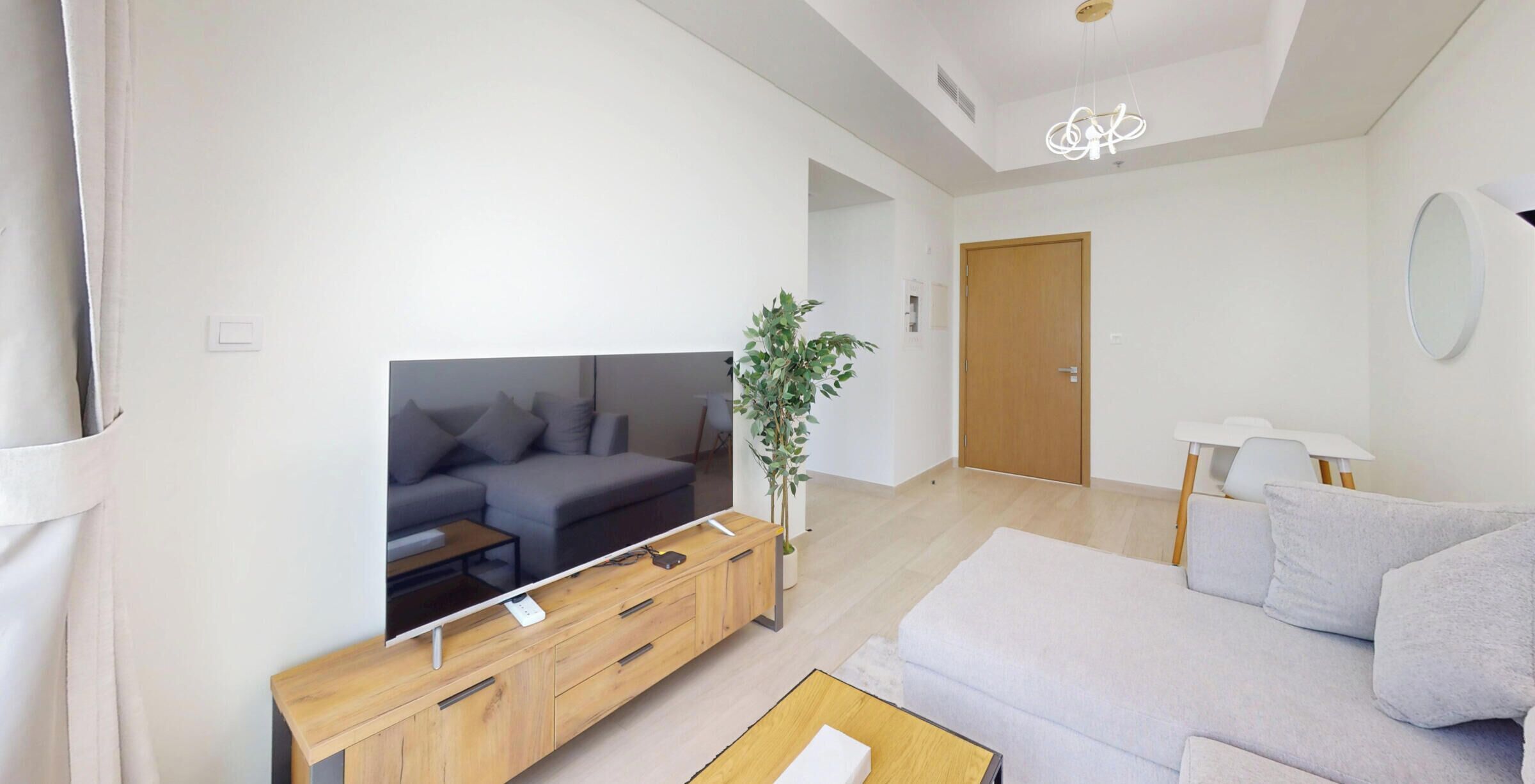 Ein modernes Wohnzimmer mit Flachbildfernseher, grauem Sofa, Holz-TV-Möbel und einem Blumentopf.