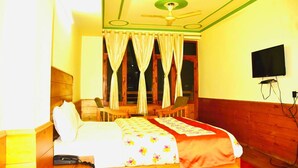 Habitación de hotel con cama, escritorio, silla, televisor y ventilador de techo.