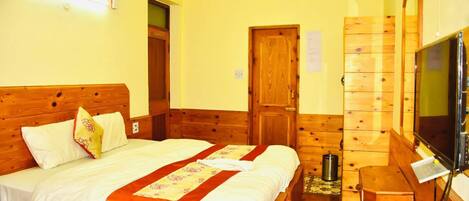 A hotel room with a wooden bed, a television, a wooden wardrobe, and a door.