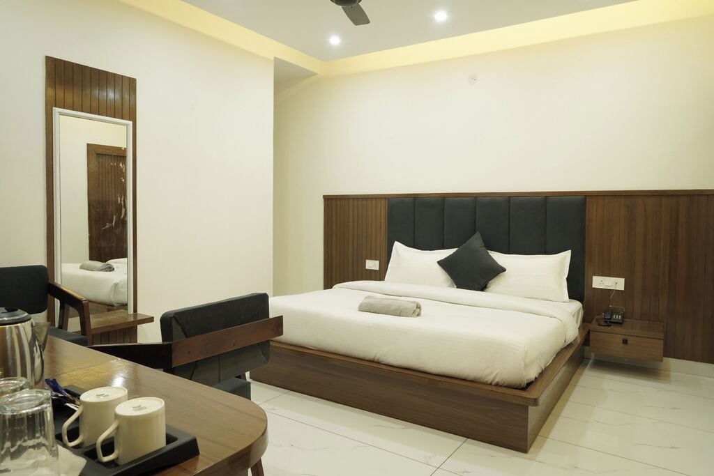 Una habitación de hotel con cama, mesitas de noche, un escritorio con silla y un espejo.