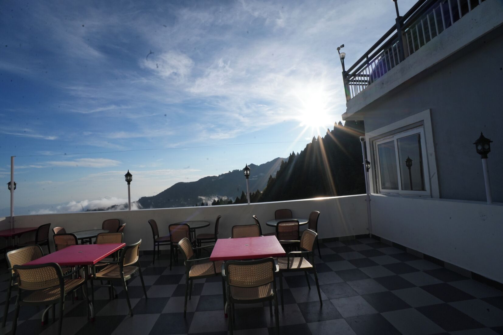 An outdoor seating area with tables and chairs, overlooking a mountainous landscape with a clear sky.
