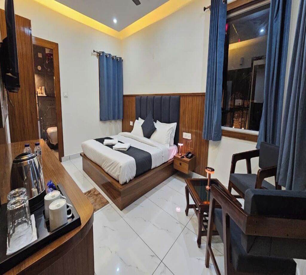 A hotel room with a bed, bedside table, lamp, chair, and a view of the outside.