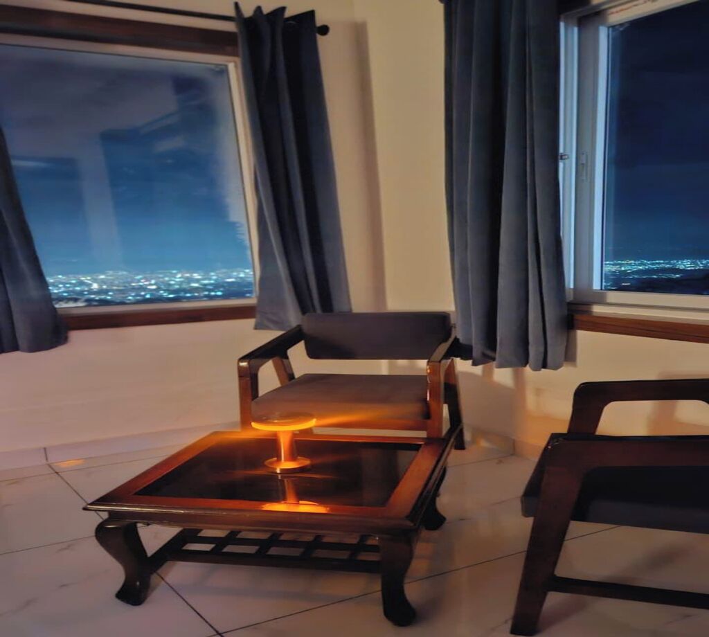 Una habitación con vistas a un paisaje urbano nocturno, una silla y una mesa con luz.