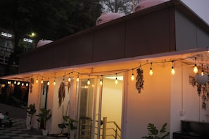 Un edificio con un espacio exterior techado, plantas en macetas y luces colgantes.