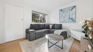 Uma sala de estar moderna com um sofá seccional cinza, uma mesa de centro, um tapete felpudo branco e um grande quadro abstrato na parede.