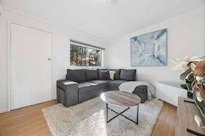Ein modernes Wohnzimmer mit einem grauen Ecksofa, einem Couchtisch, einem weißen Shaggy-Teppich und einem großen abstrakten Gemälde an der Wand.