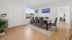 Uma área de refeições com mesa e cadeiras, um relógio na parede e uma janela com vista para edifícios.