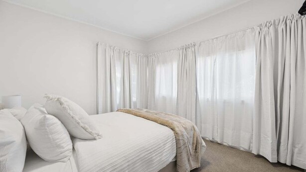 Quarto com cama, almofadas, mesa de cabeceira e cortinas.