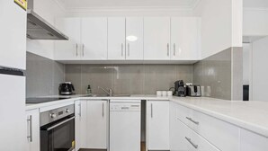 Uma cozinha moderna com armários brancos, lava-louças, forno e cafeteira.