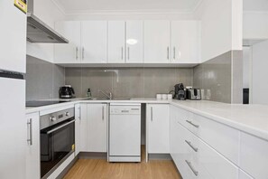 Eine moderne Küche mit weißen Schränken, einem Geschirrspüler, einem Backofen und einer Kaffeemaschine.