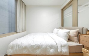 Une chambre à coucher avec un lit, une table de chevet en bois, un miroir et une fenêtre avec des rideaux.