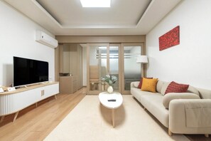 Un salon moderne avec un téléviseur à écran plat, une table basse blanche, un canapé beige agrémenté de coussins et une œuvre d’art rouge accrochée au mur.