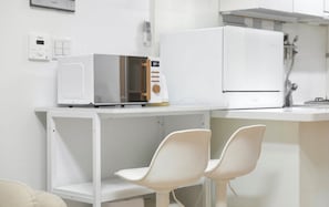 Une cuisine équipée d’un four à micro-ondes, d’un réfrigérateur et de deux chaises blanches.