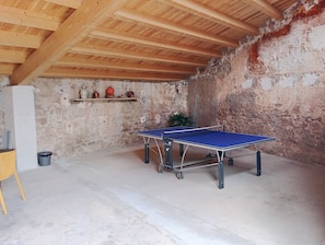 A ping pong table in a room with a rustic stone wall and wooden beams.