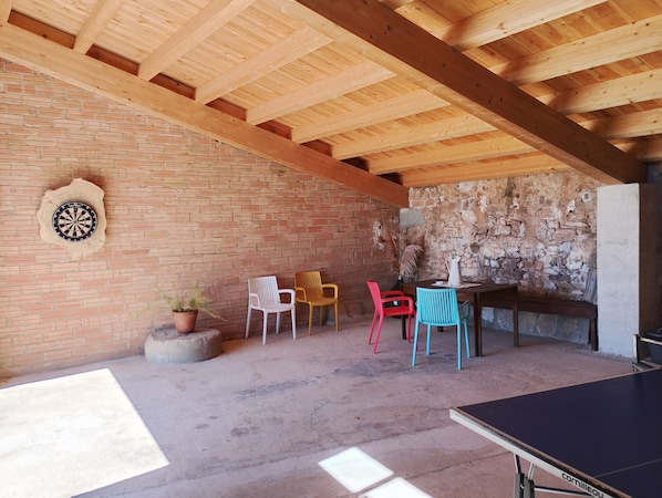 A room with a dartboard, a table, chairs, and a ping pong table.