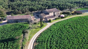 A stone farmhouse with a tiled roof, surrounded by a lush green field and a forested hill in the background.