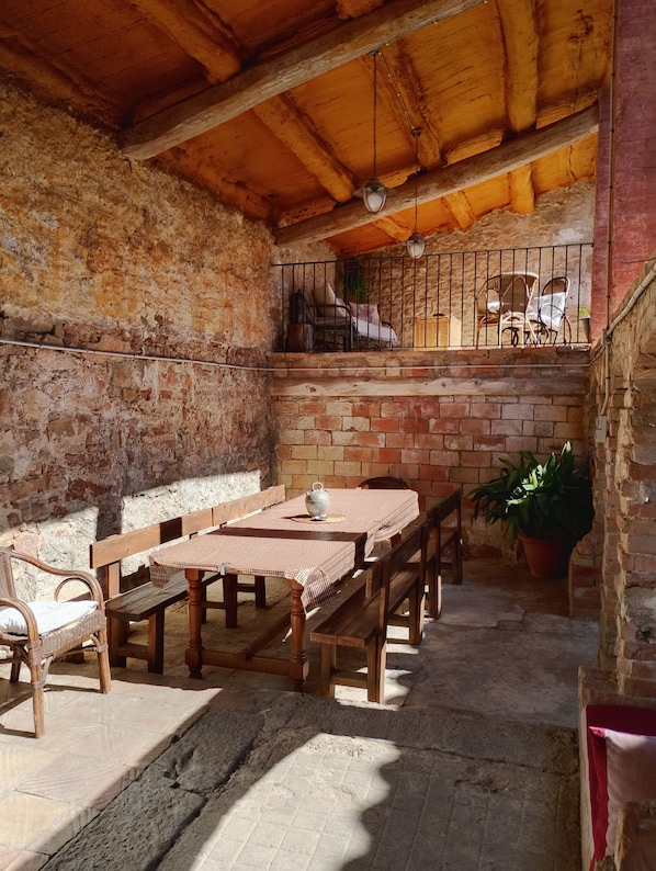 A rustic outdoor dining area with a brick wall, wooden furniture, and a balcony with chairs.