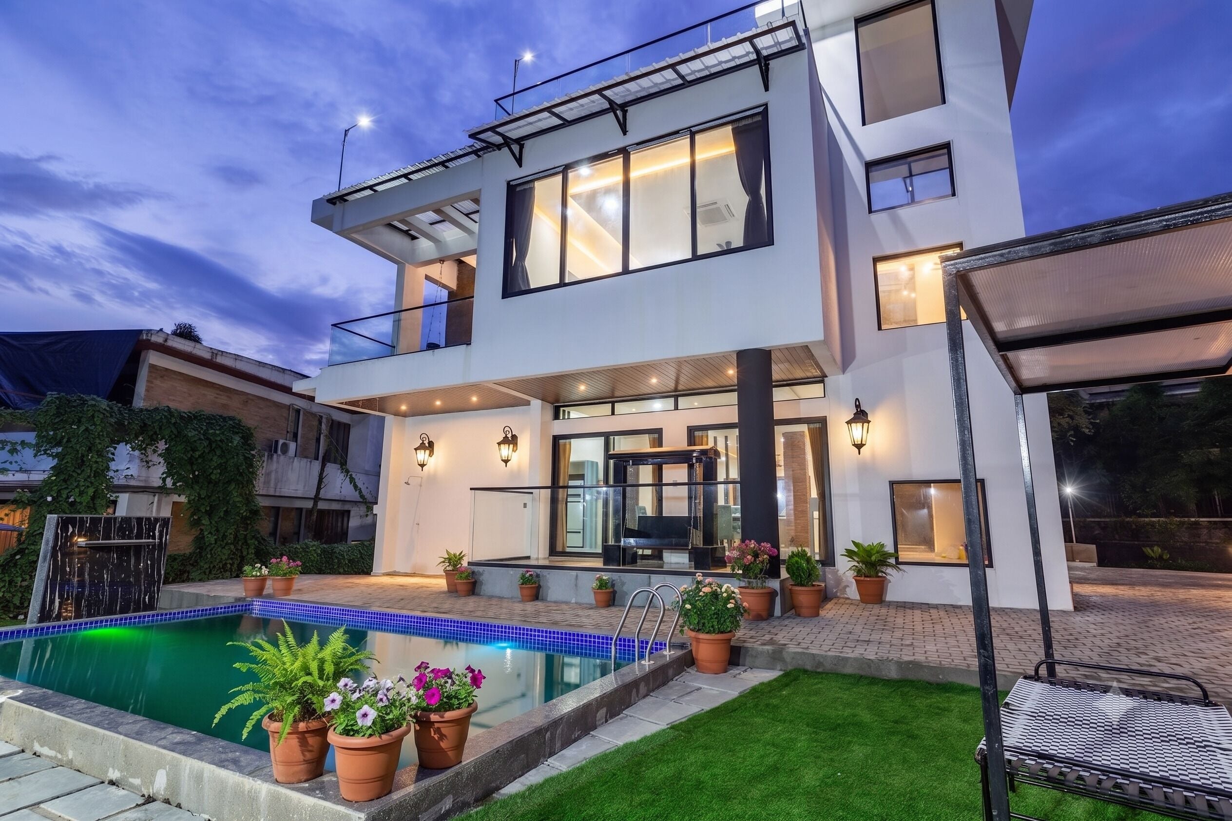 A modern two-story house with a swimming pool, outdoor seating, and potted plants.