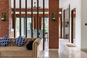 Um interior moderno com parede de tijolos, um sofá com almofadas estampadas, um ventilador de teto e vista através de amplas janelas.