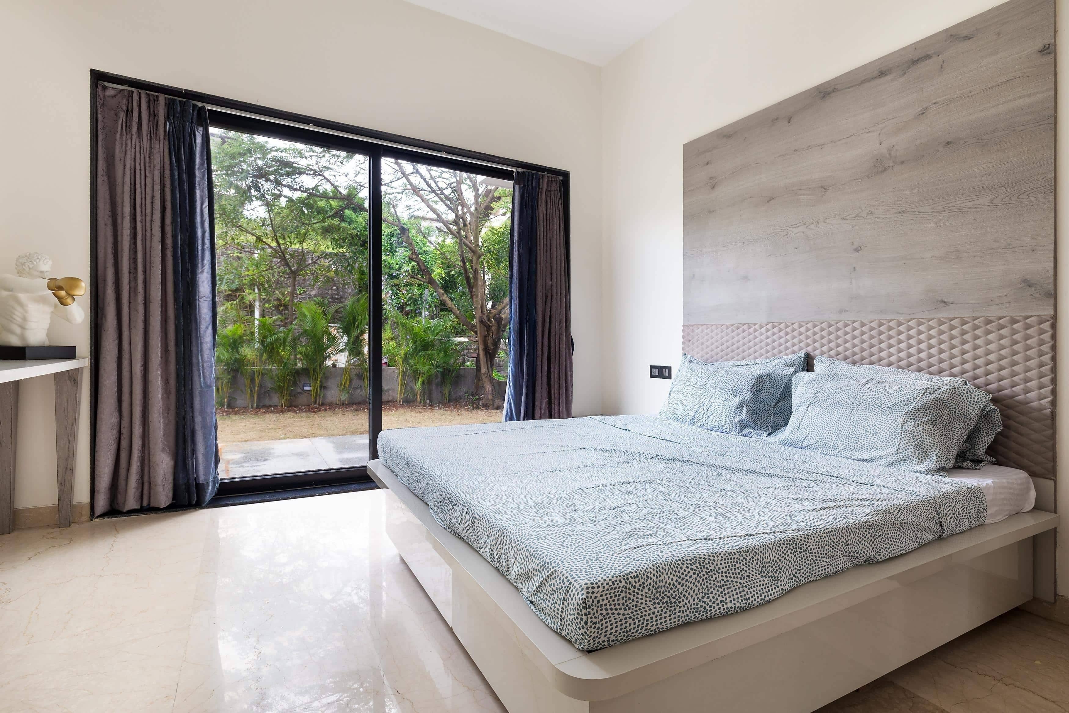 A bedroom with a bed, a nightstand, and a view of a garden through a sliding door.