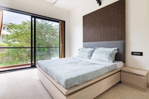 Quarto moderno com uma cama grande, vista para o verde lá fora e cabeceira de madeira.