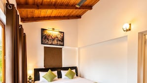 A bedroom with a wooden ceiling, a bed with a green throw, a nightstand with a lamp, and a wall-mounted picture.