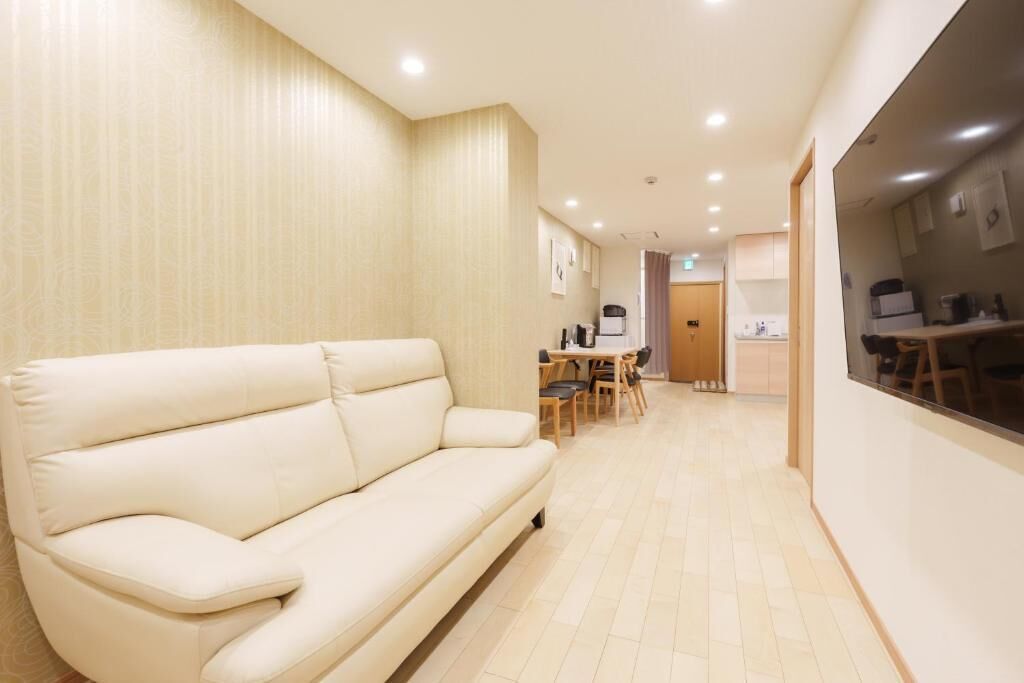 A modern hotel room with a sofa, a dining area, and a kitchenette.