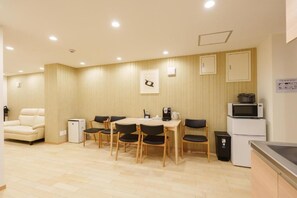 A compact hotel room with a dining area, a sofa, a microwave, a refrigerator, and a small cabinet.