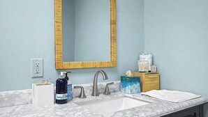 Un baño con lavamanos de mármol, un espejo grande con marco dorado y artículos de aseo en la encimera.