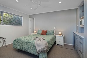 Ein Schlafzimmer mit Bett, Nachttischen, Deckenventilator, Fenster mit Jalousien und einem Einbauschrank.