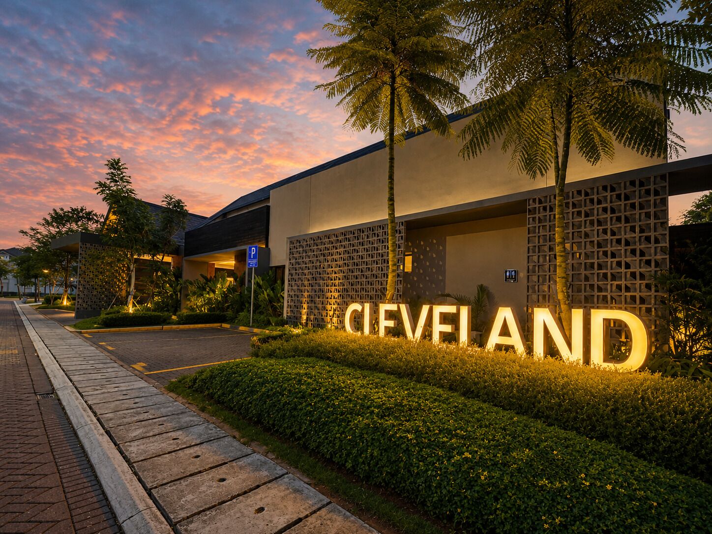 A hotel entrance with a large illuminated sign, a paved walkway, and landscaped greenery.