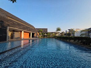 Una piscina con solárium de baldosas, rodeada de edificios de arquitectura moderna.