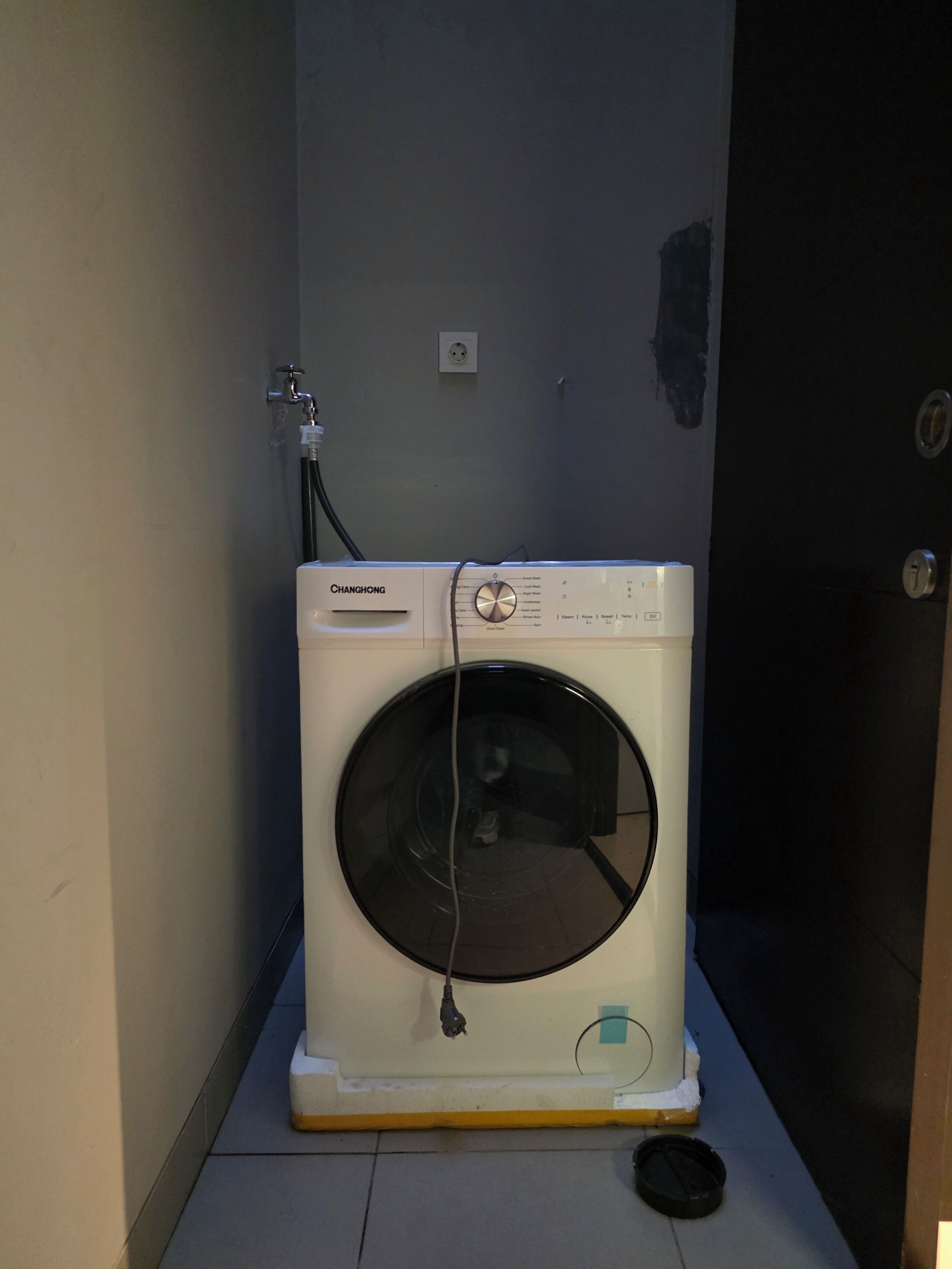 Lavadora blanca compacta con panel de control, ubicada en un espacio reducido con piso de baldosas.
