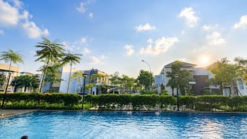 Una piscina con dos personas nadando, rodeada de follaje y edificios.